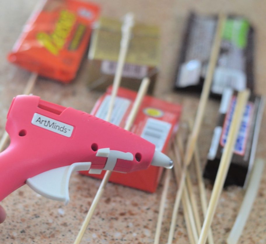 demonstrating how to make a candy bouquet by using a hot glue gun to stick candy to skewers