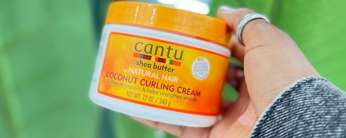 hand holding up an orange jar of Cantu Coconut Curling Cream