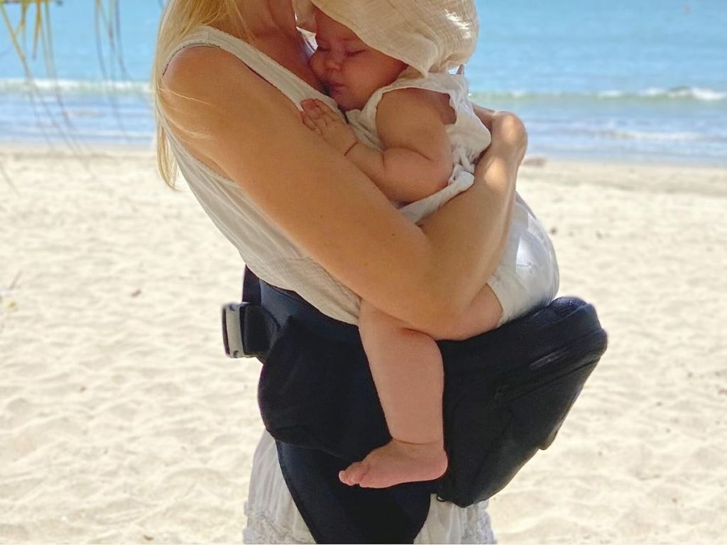 A woman wearing a CozyOne Baby Hip Carrier