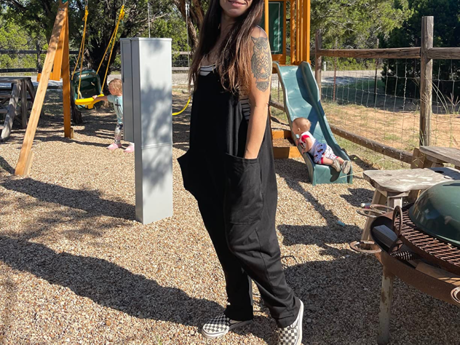 A woman on a playground wearing a DEEP SELF Sleeveless Jumpsuit in black