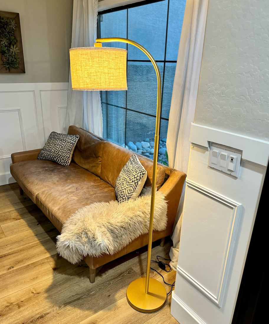 gold arch lamp next to brown leather sofa