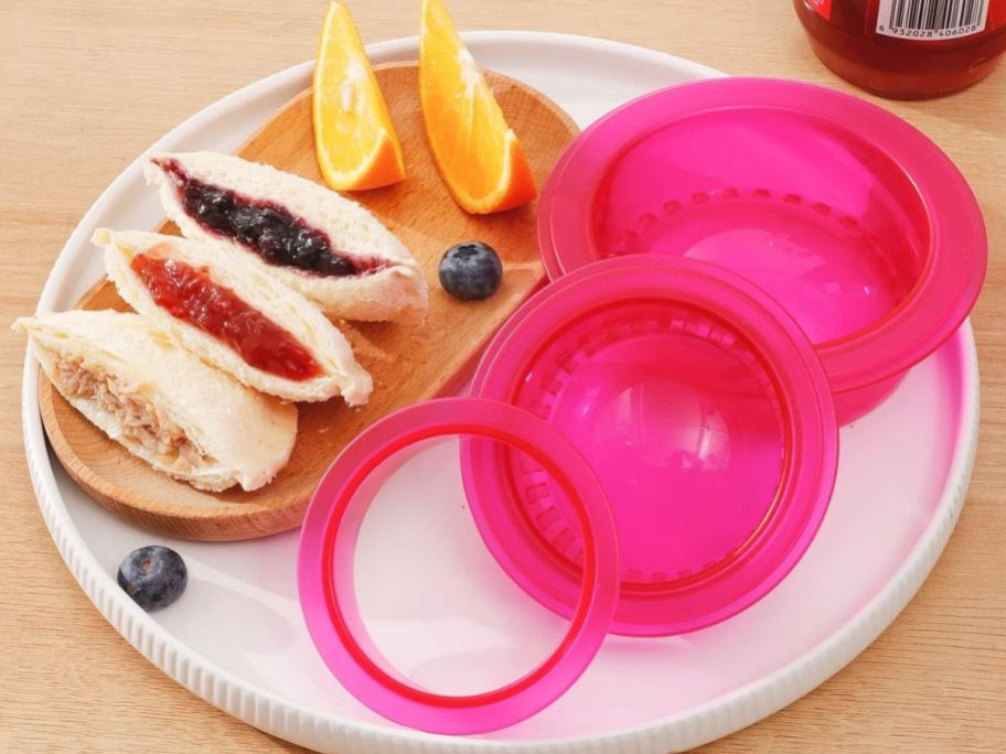 ADarsun Uncrustable Sandwich Cutter in pink on a plate surrounded by sandwiches and food