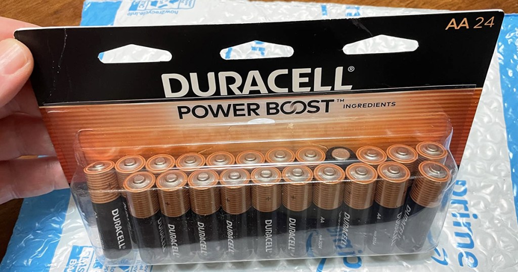 hand holding a pack of Duracell Coppertop AA Batteries on top of a prime shipping package