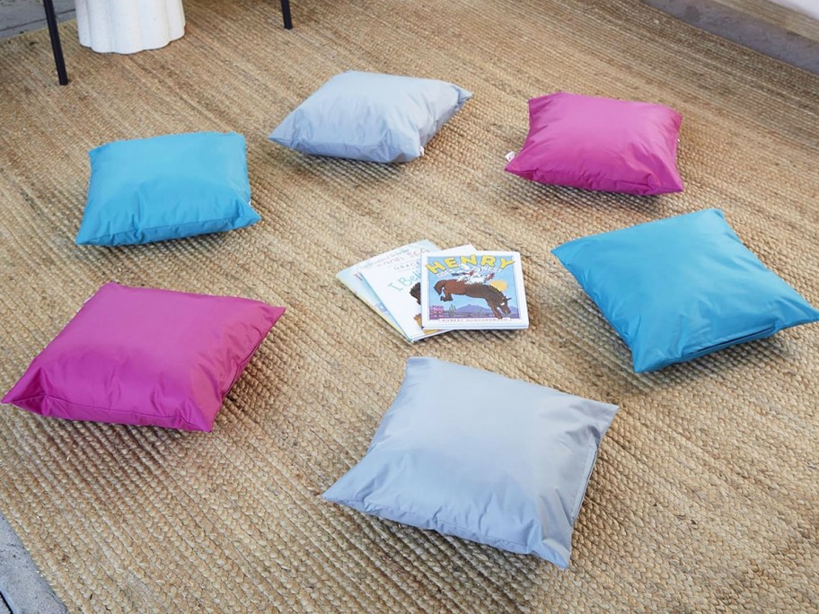 grey, blue, and maroon floor pillows in a circle around stack of books