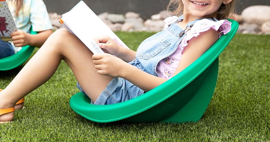 girl sitting in green plastic rocker chair on grass