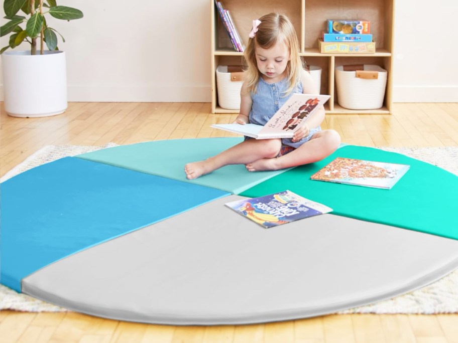 girl reading book on a blue, green, and grey round activity mat