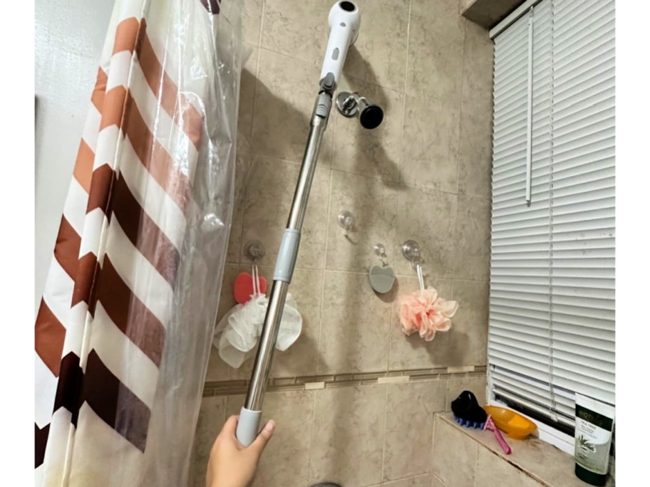 person cleaning tile shower with long Electric Scrubber 