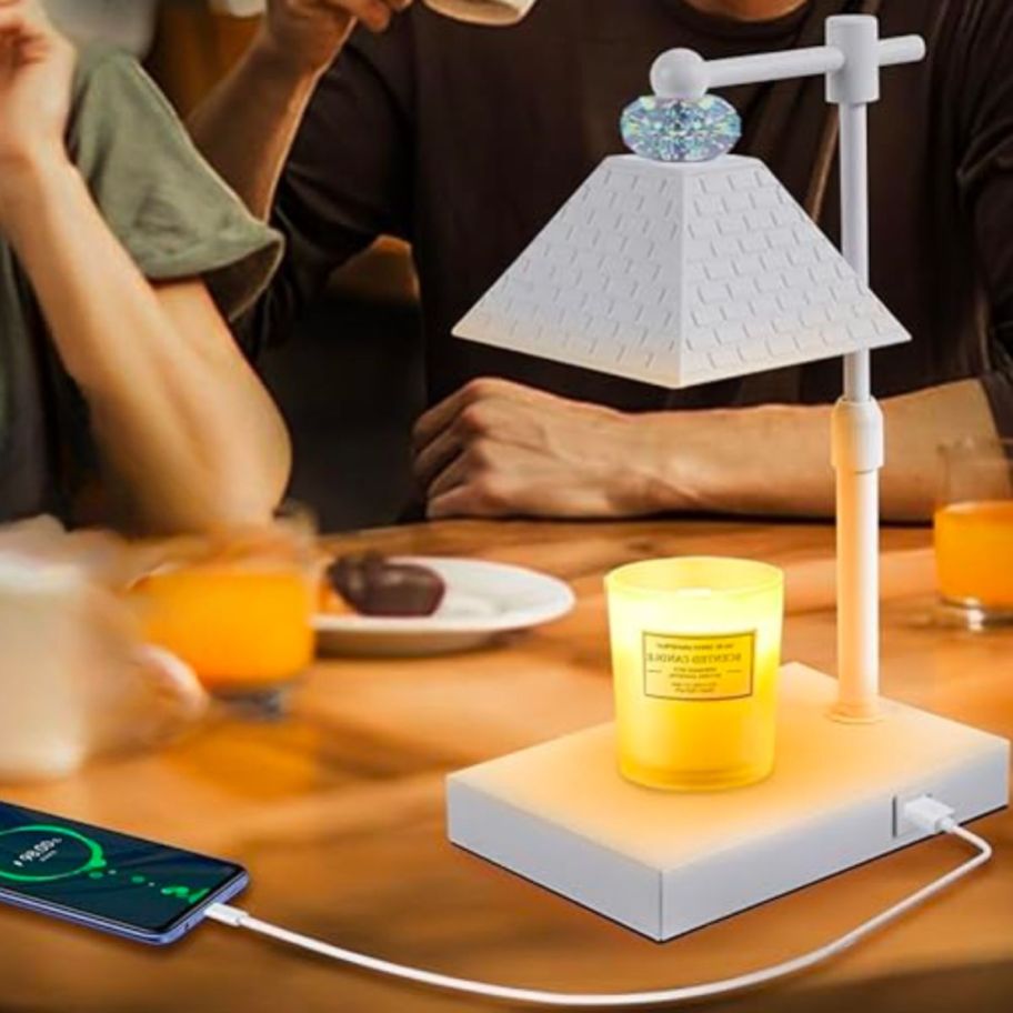 a white candle warmer lamp sitting on a table with a smart phone plugged into its base charging