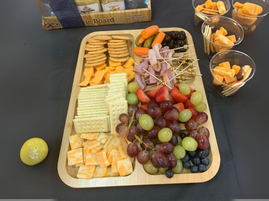 FARBERWARE Build-a-Board Cutting Board with Compartments and Clear Locking Lid for Charcuterie with fruit and cheese on it