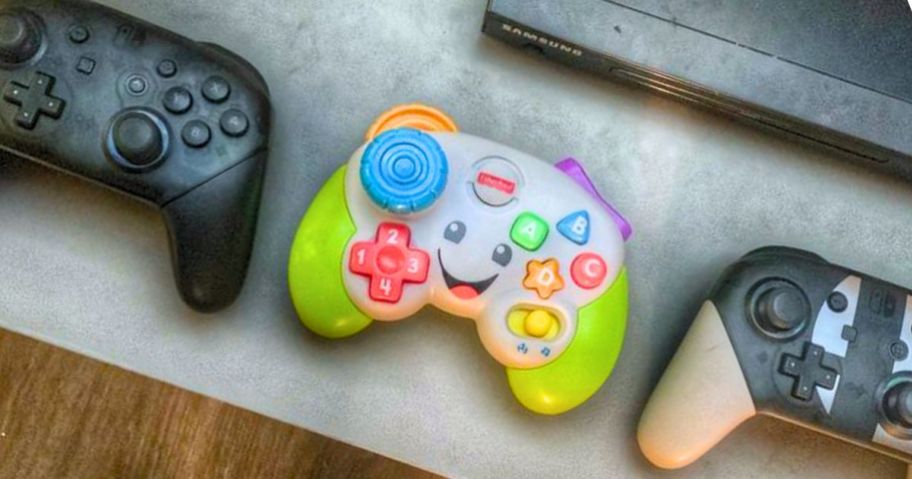 a colorful pretend kids game controller next to 2 adult game controllers on a table
