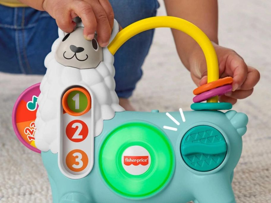 Baby hand touching the head of a Fisher Price Linkimals Llama toy