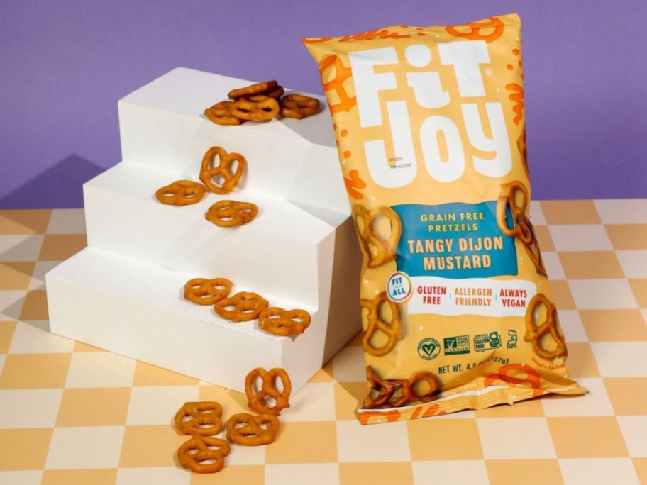 A bag of Fit Joy Honey Mustard Pretzels next to a mini staircase with some of the pretzels on it