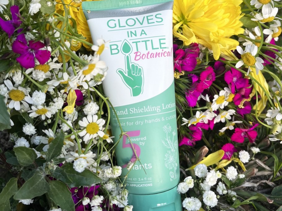 Gloves in a Bottle Botanical Hand Shielding Lotion tube on top of colorful flowers