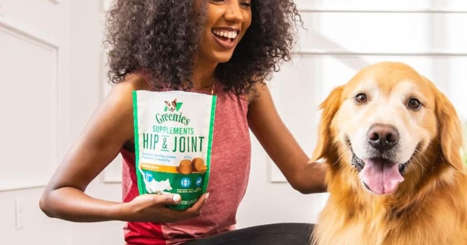 person holding Greenies hip and joint supplements standing next to dog