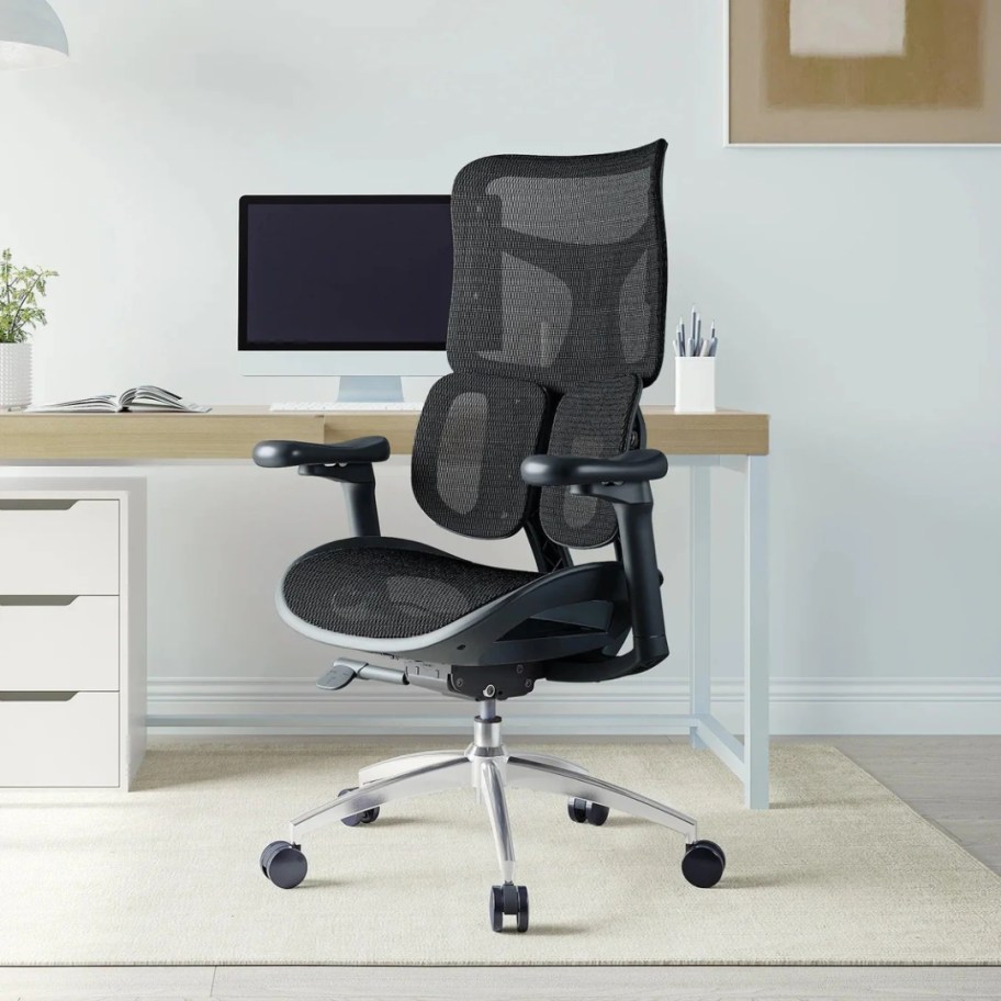 a tall black mesh and ergonomic desk chair with wheels at a desk