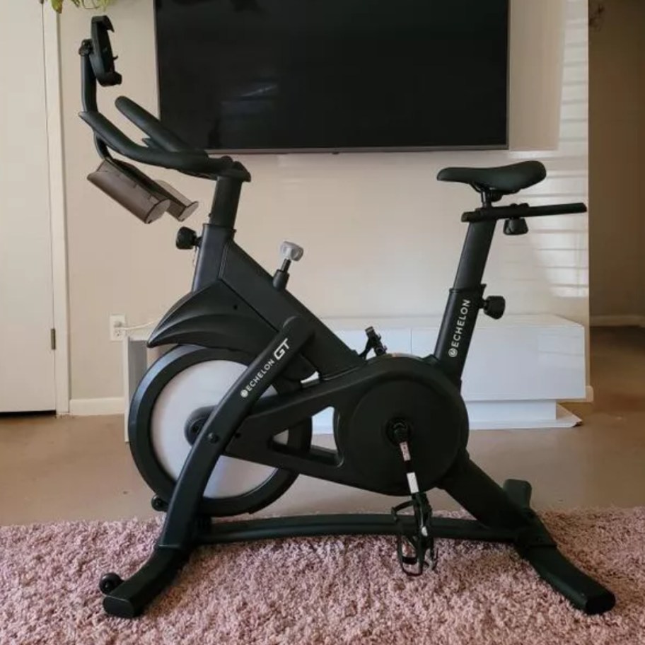 black indoor exercise bike in a living room, TV on wall behind it