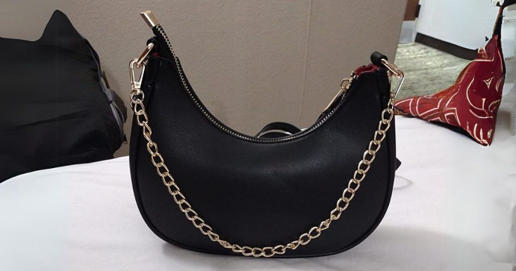 black crescent shaped women's handbag with a gold chain accent sitting on bed