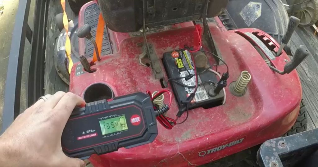 person's hand holding a 10A 6V/12V battery charger that's hooked up to a lawn mower