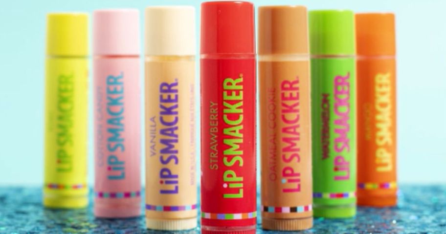 various flavors of colorful lip smacker lip balms standing up on a blue background