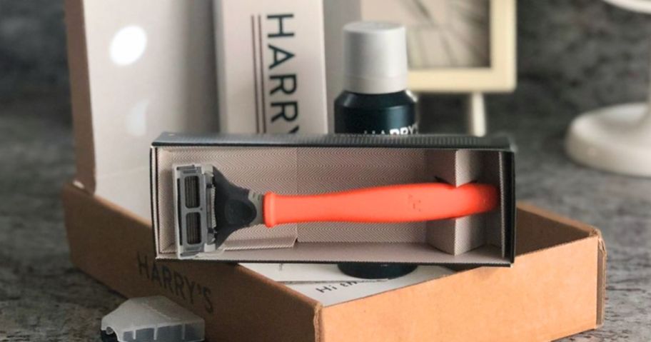 orange Harry's razor sitting on a box with a shave kit with shave gel and lotion and the packaging