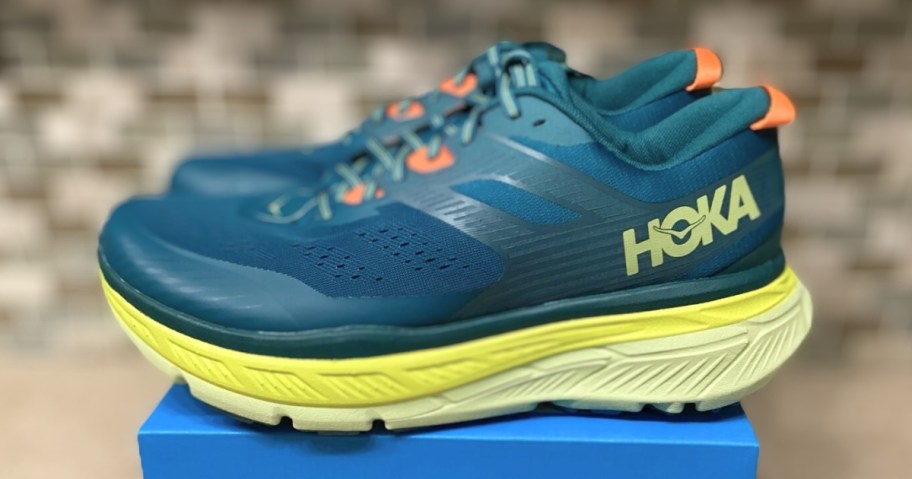 dark teal blue, yellow and orange HOKA running shoes sitting on blue shoe box