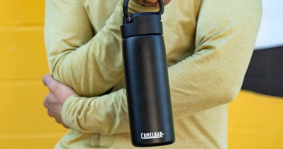 man holding a black CamelBak water bottle standing against a yellow wall