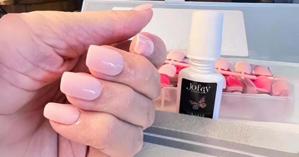woman's hand shown with light pink Jofay press on nails, nail kit and glue behind her hand
