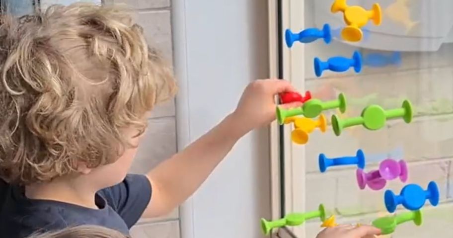 little boy playing with bright color sensory suction toys on a window