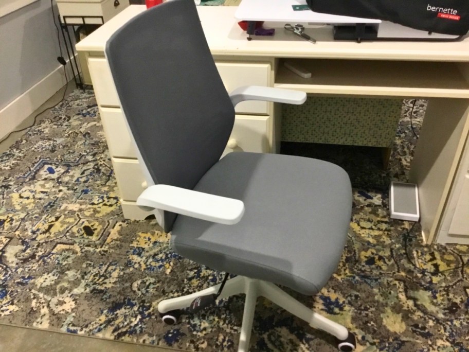 a grey and white curved desk chair with wheels by a desk