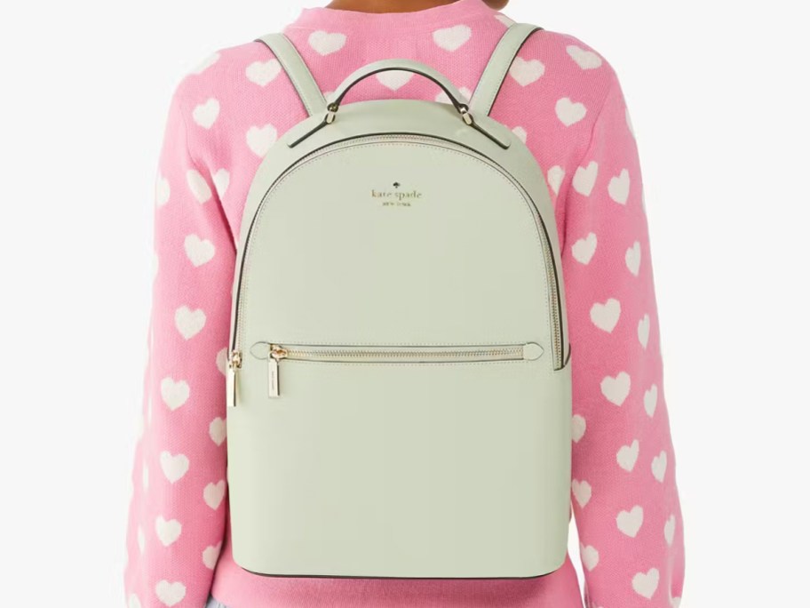 woman wearing pink heart-print sweater and light green kate spade backpack