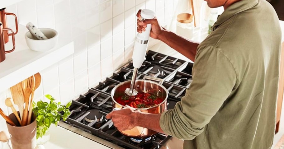 man using white hand blender in pot on stove