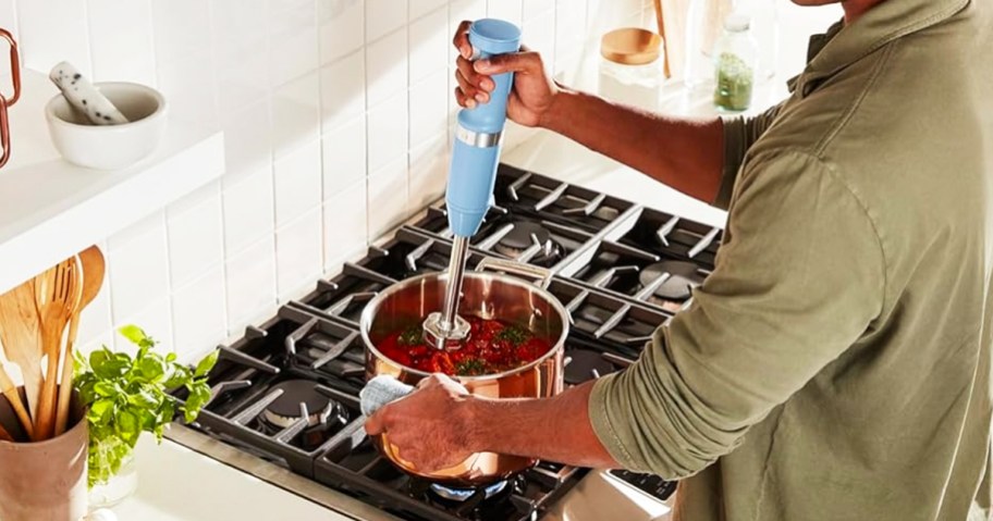man using light blue hand blender in pot on stove