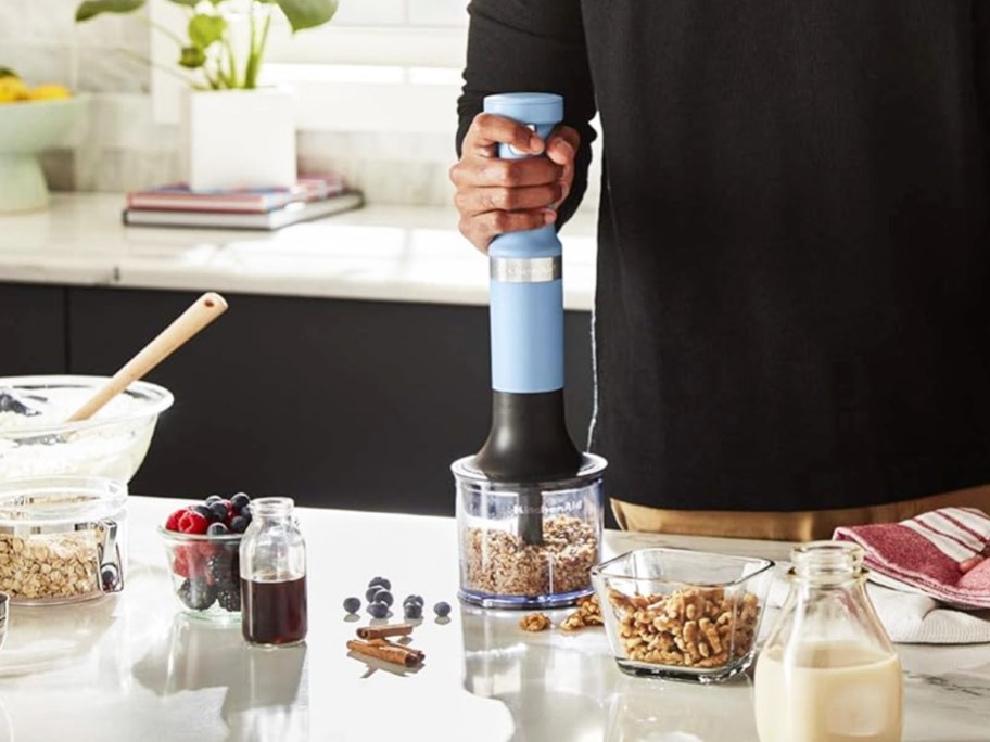 man using blue hand blender to chop nuts