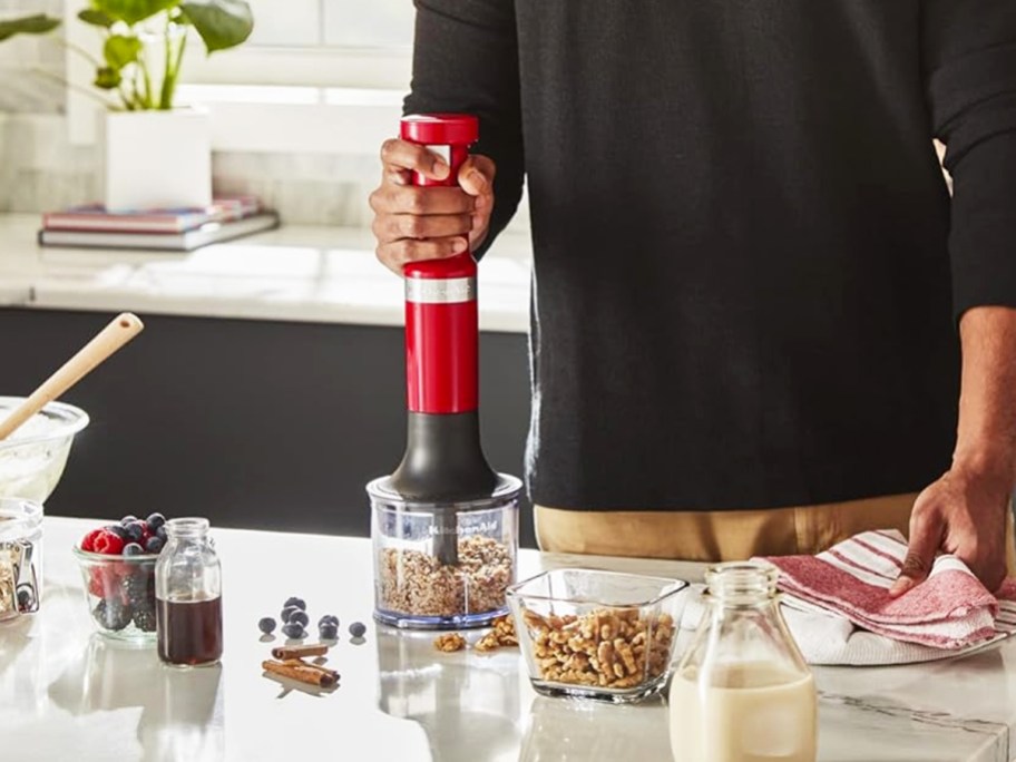 man using red hand blender to chop nuts