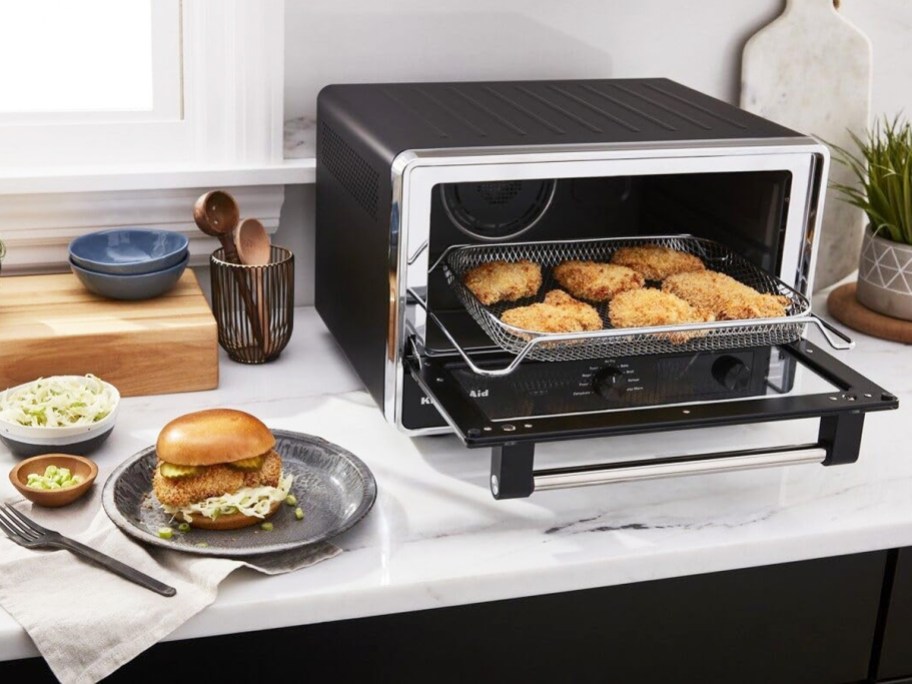 silver and black countertop oven with door open and breaded chicken inside