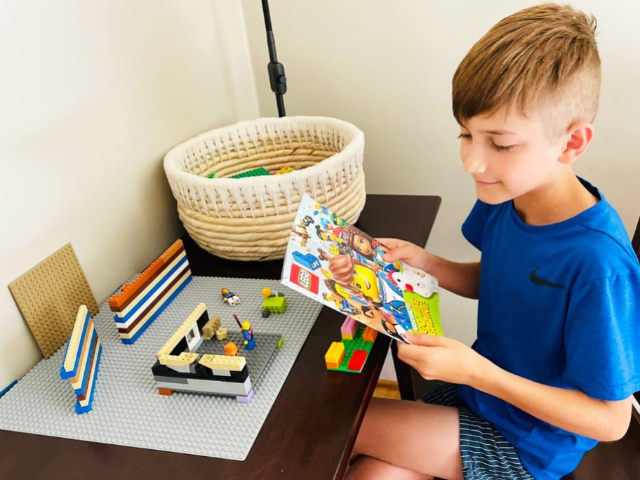 boy reading lego magazine in front of lego creations on desk