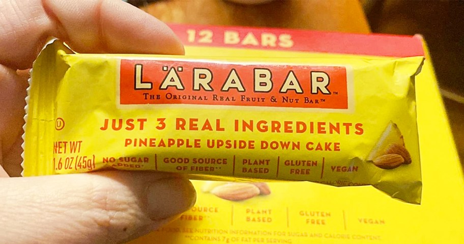 hand holding a yellow Larabar Pineapple Upside Down Cake snack bar