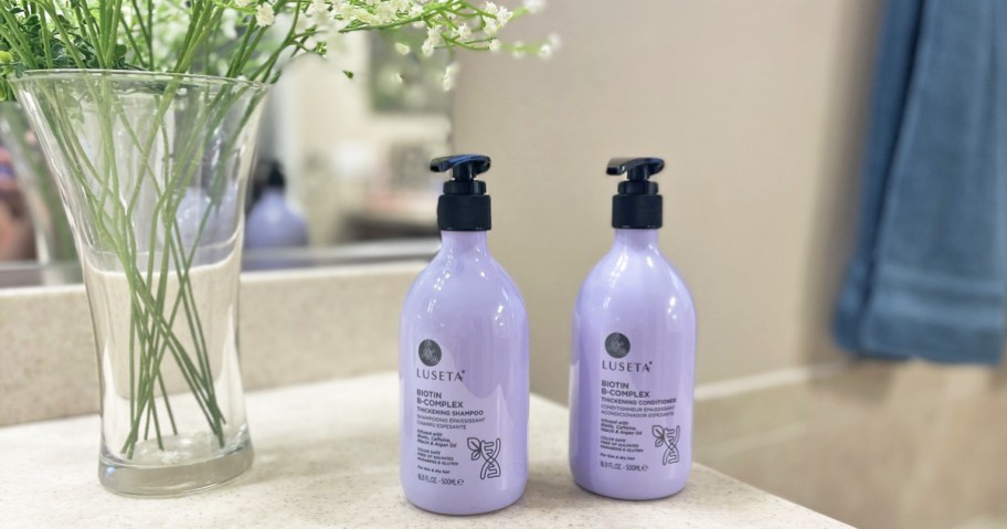 purple bottles of shampoo & conditioner on bathroom counter near flowers