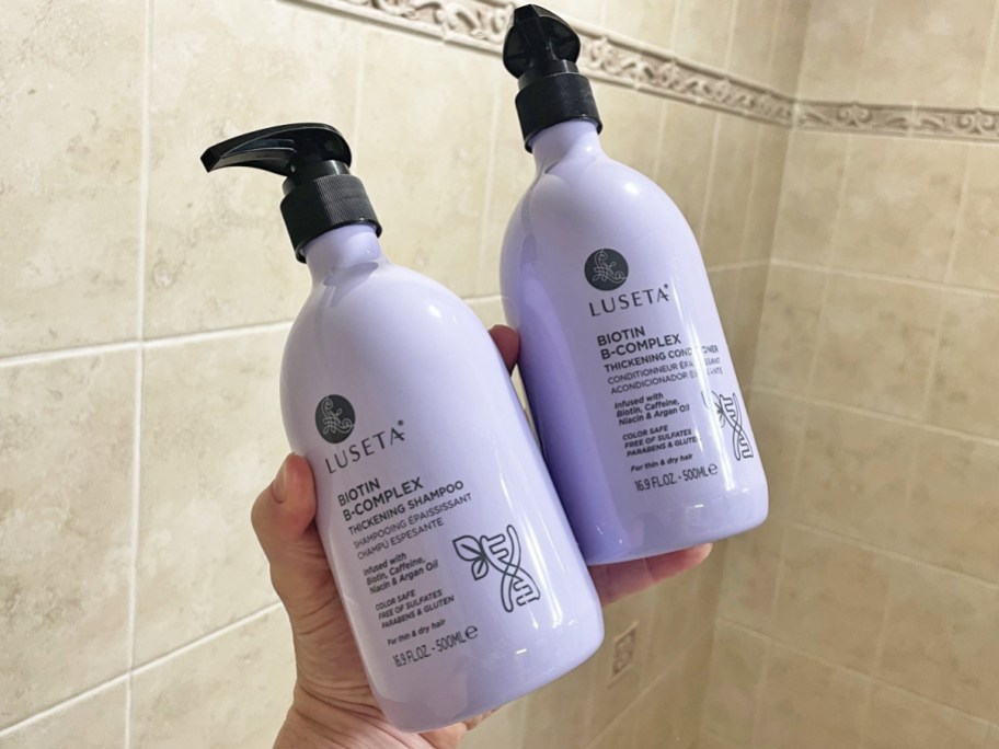 hand holding purple bottles of shampoo &conditioner in shower