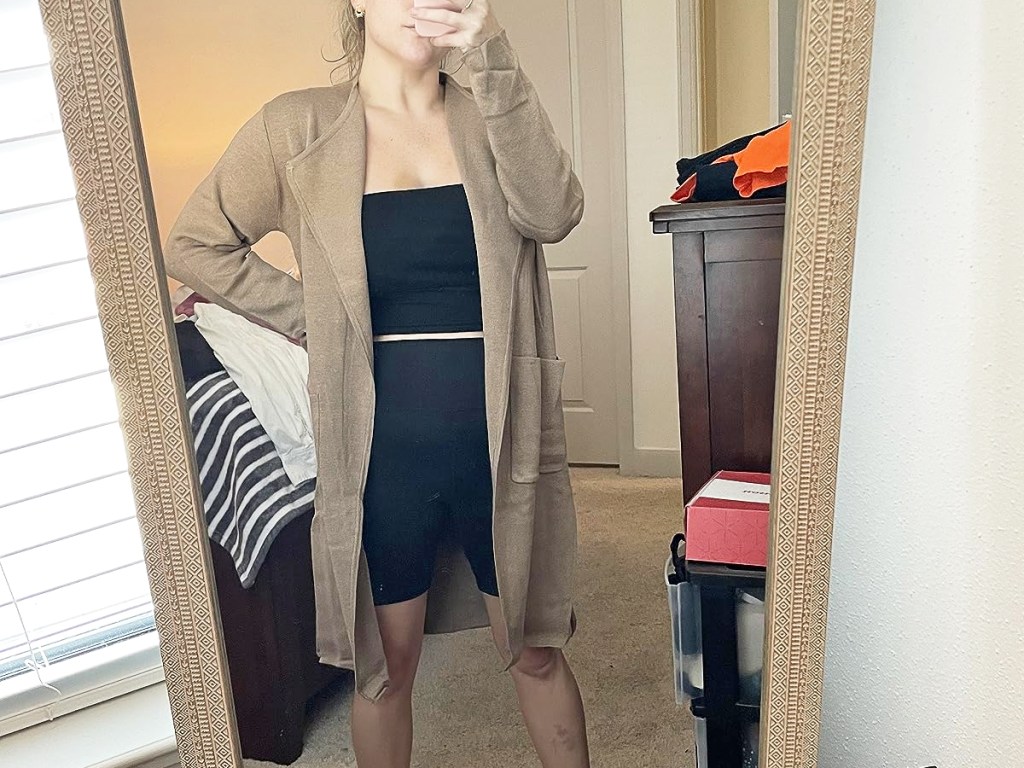 Frau macht ein Selfie im Spiegel und trägt einen braunen Mantel