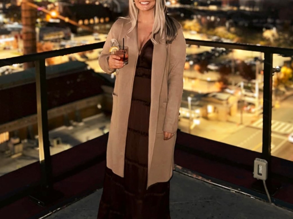 woman standing on balcony at night holding a drink