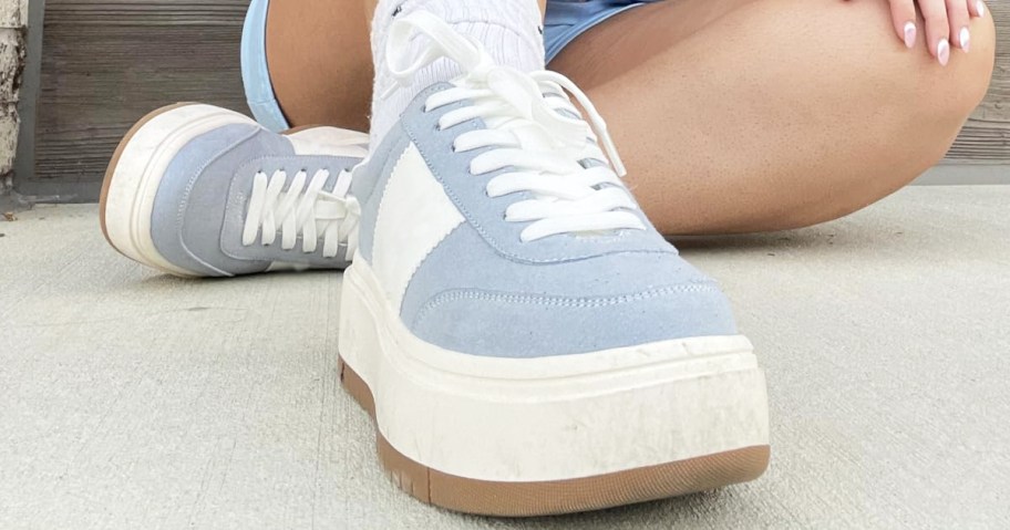 woman sitting on ground wearing blue and white platform sneakers