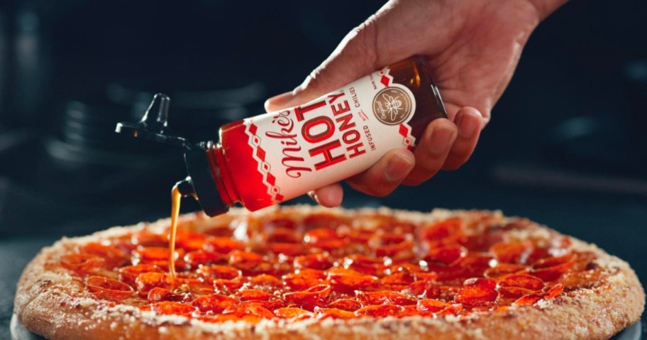 person pouring mike's hot honey on pepperoni pizza