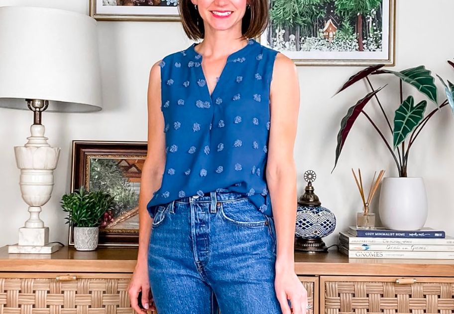 woman in a blue tank top and jeans standing in front of a console table