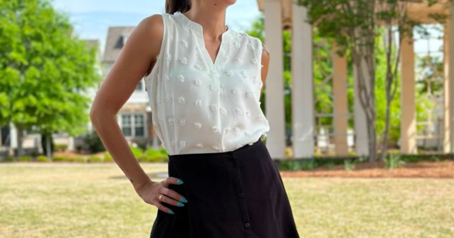 a woman in a white tank top and black skirt standing outside