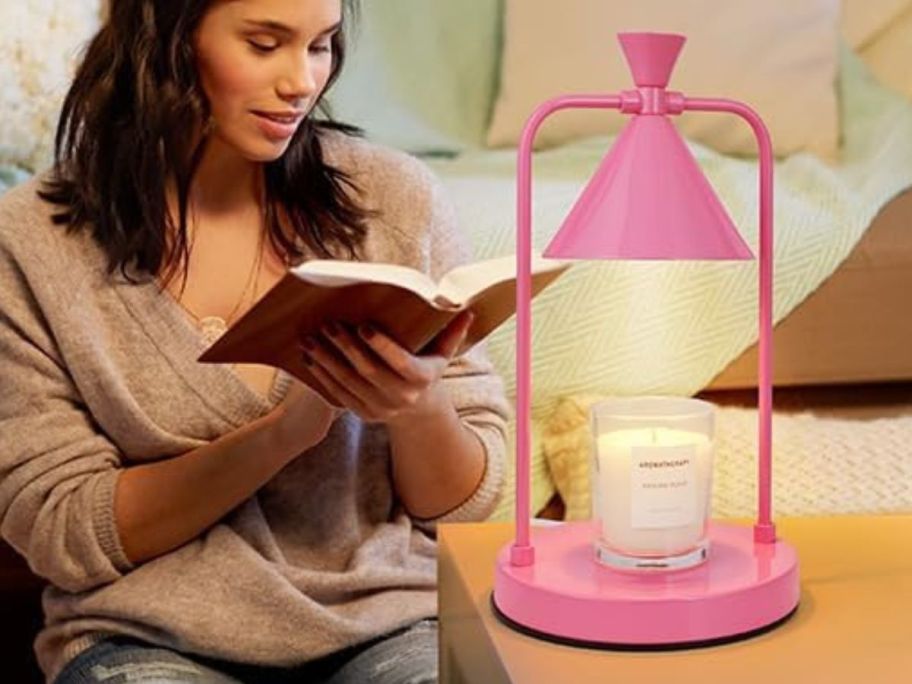A woman reading a book next to a pink candle warmer