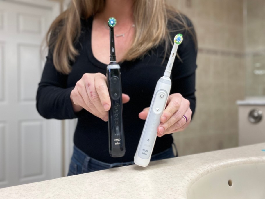 Woman holding two Oral B Genius electric toothbrushes