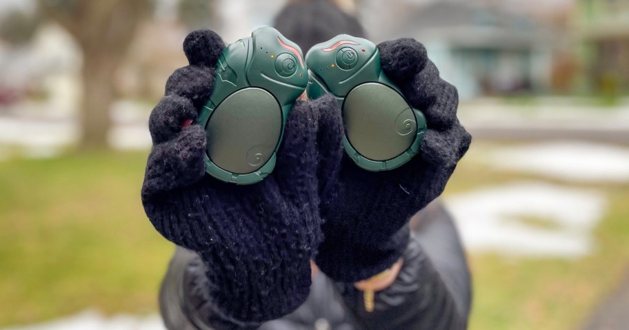 hands in black mittens holding green rechargeable hand warmers