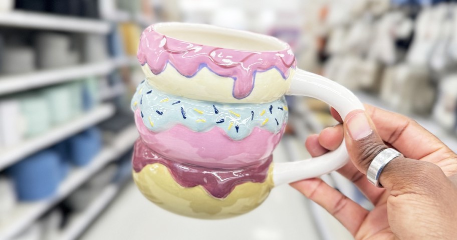 hand holding a coffee mug shaped as a stack of donuts