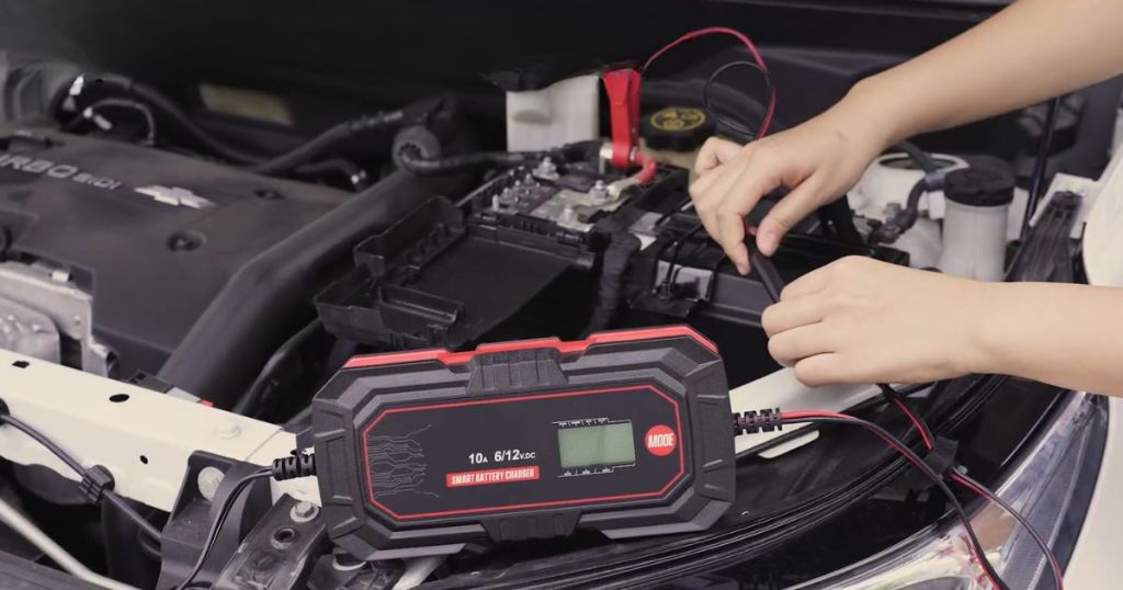 person's hands connecting the cables from a battery charger to a car battery